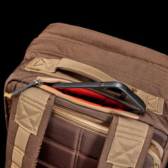 GORUCK brown rucksack with padded straps, open zipper pocket holding a smartphone
