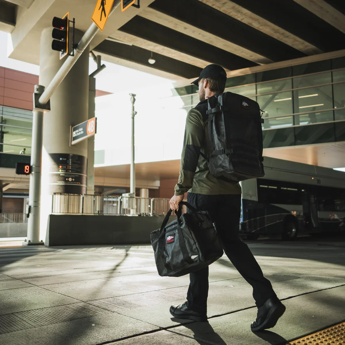 Man with GORUCK backpack and bag walking at urban transit station, tough travel gear