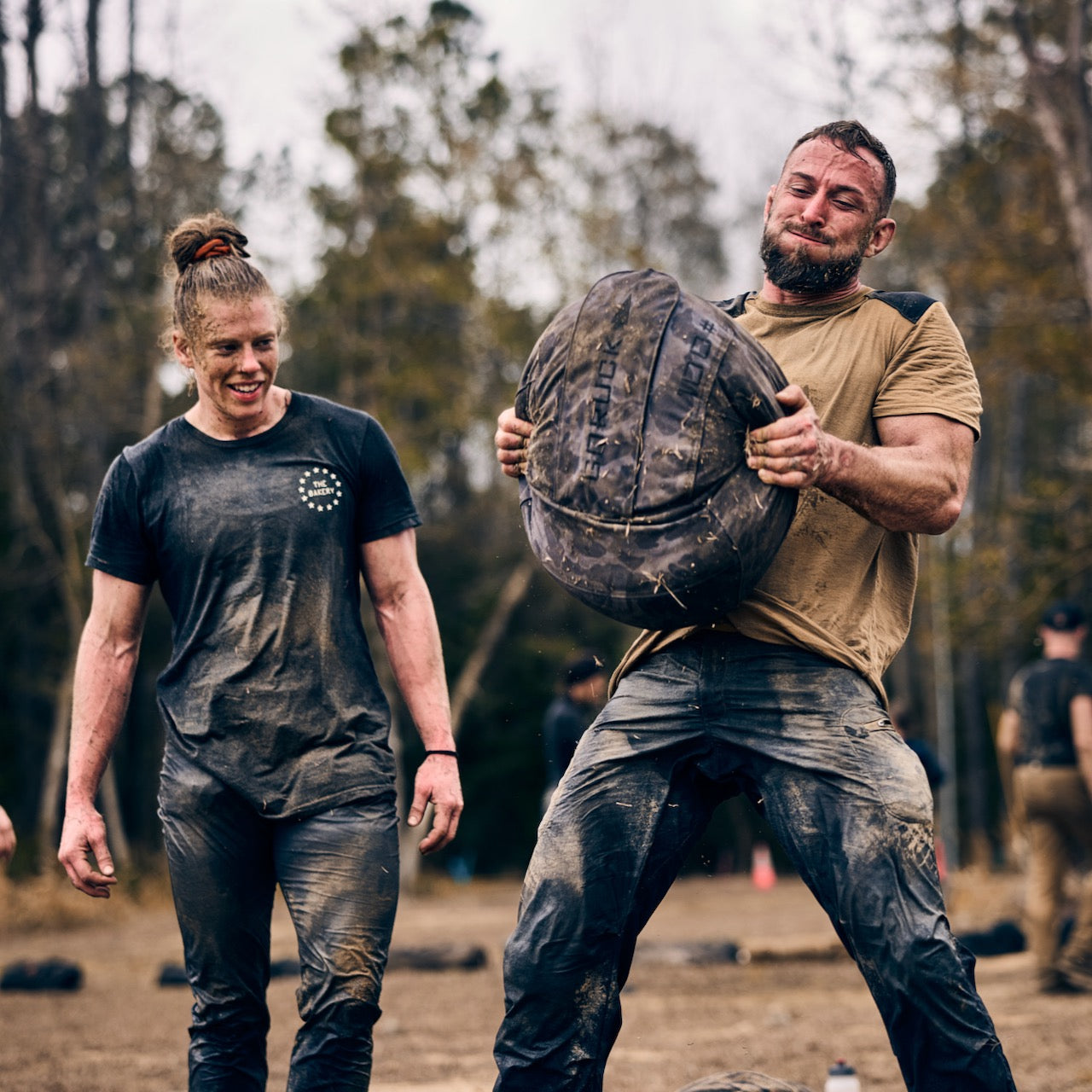 During an outdoor fitness challenge, two participants are covered in mud while using the Sand Medicine Ball to test their core strength.