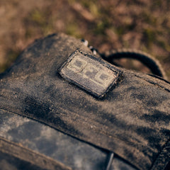 A close-up of a dirt-covered fabric bag with a worn "DFQ" embroidered patch on it.