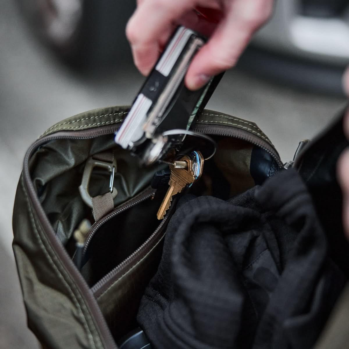 Hand placing keys and multitool into GORUCK rucksack with gear inside