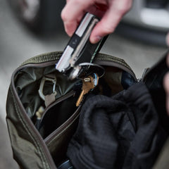 Hand placing keys and multitool into GORUCK rucksack with gear inside