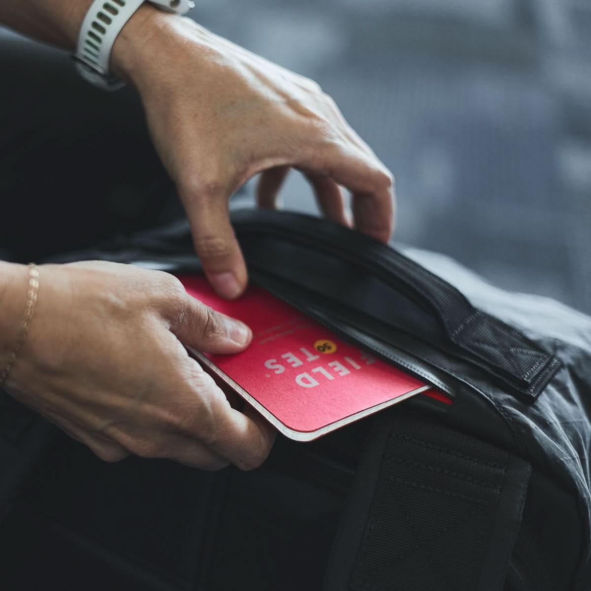 Hand placing red Field Notes notebook into durable GORUCK rucksack front pocket