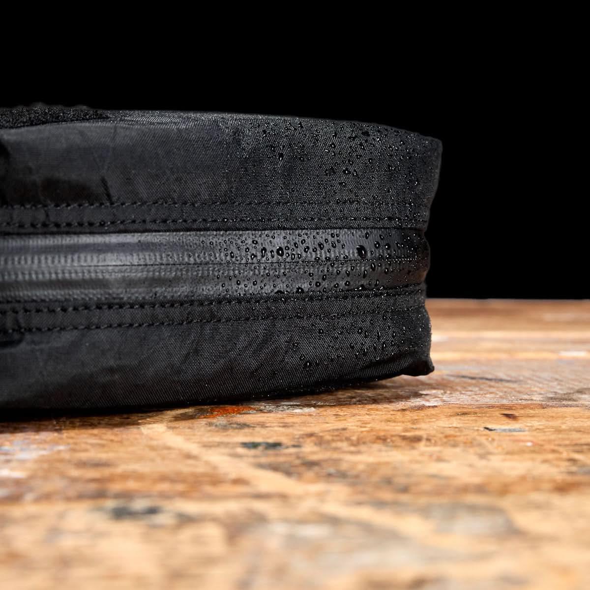 Close-up of GORUCK black rucksack with water-resistant zipper and droplets on wood table