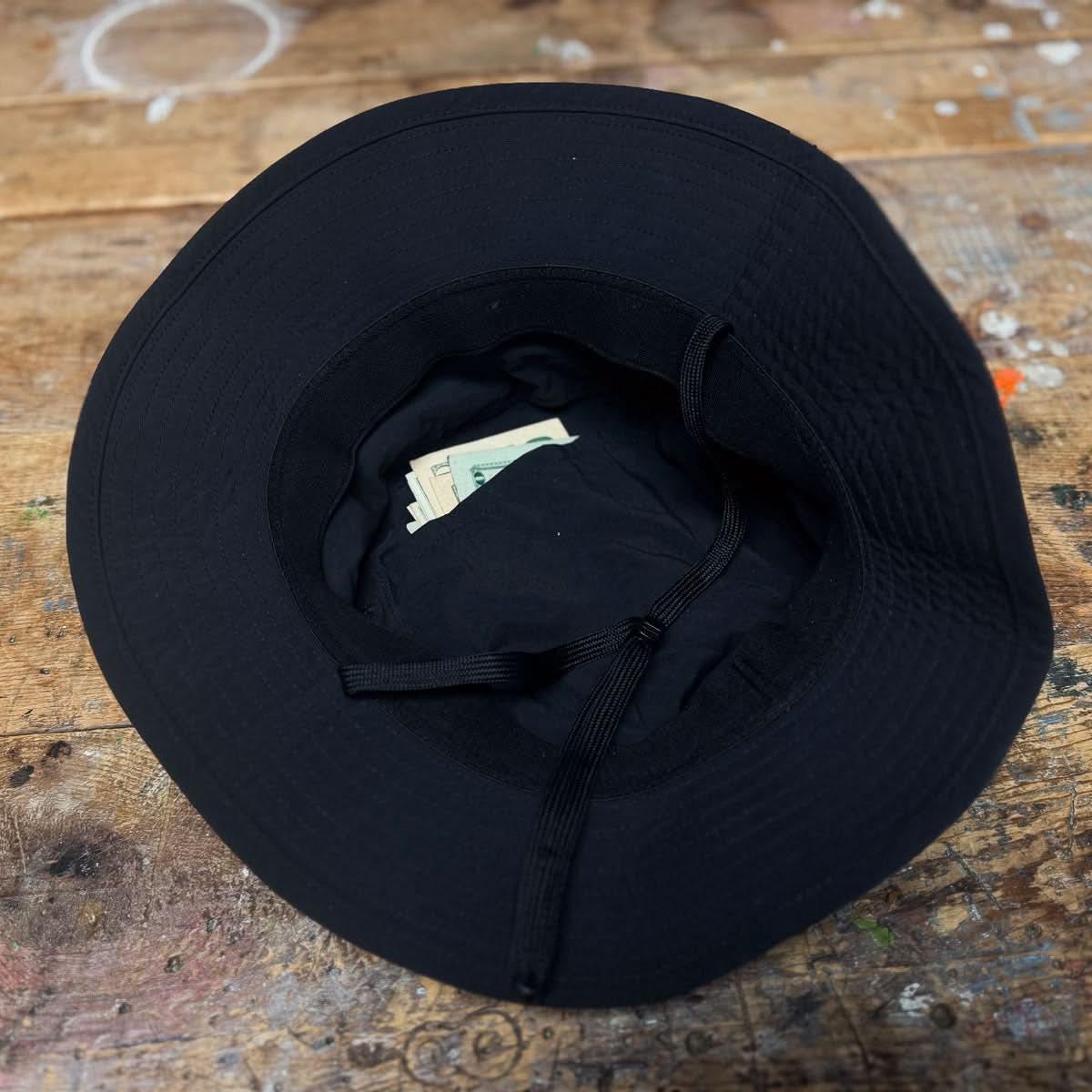 GORUCK black boonie hat with interior pocket holding cash on a wooden surface