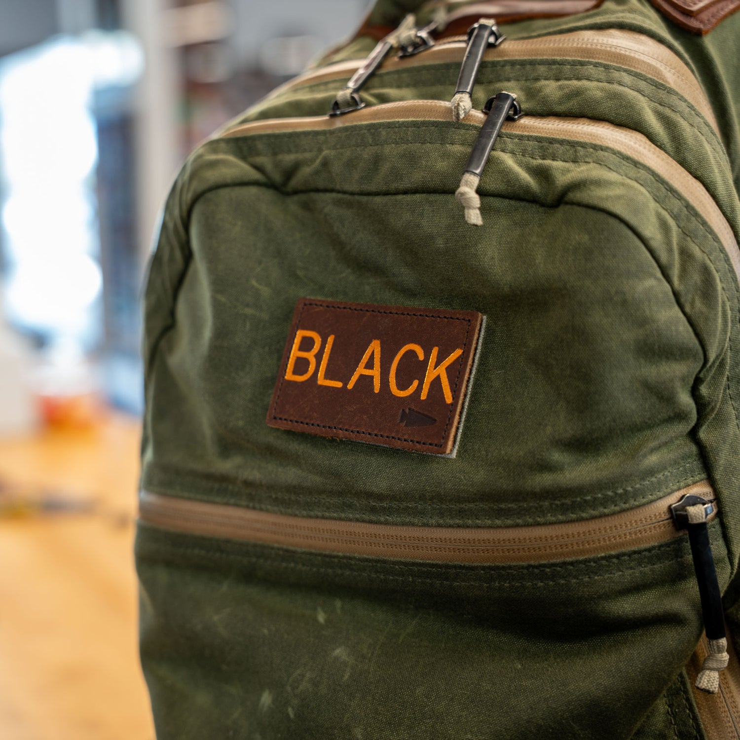 A green backpack features a brown Custom Leather Monogram Patch labeled 