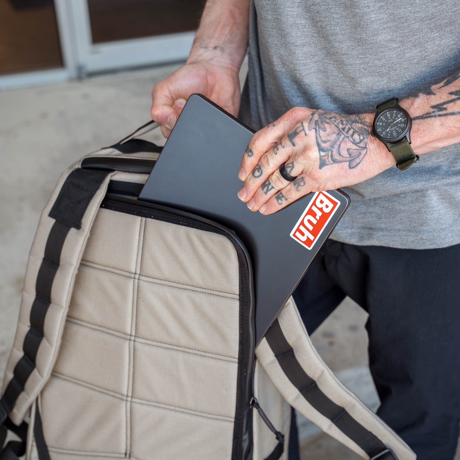 A tattooed person with a watch puts a laptop featuring a 