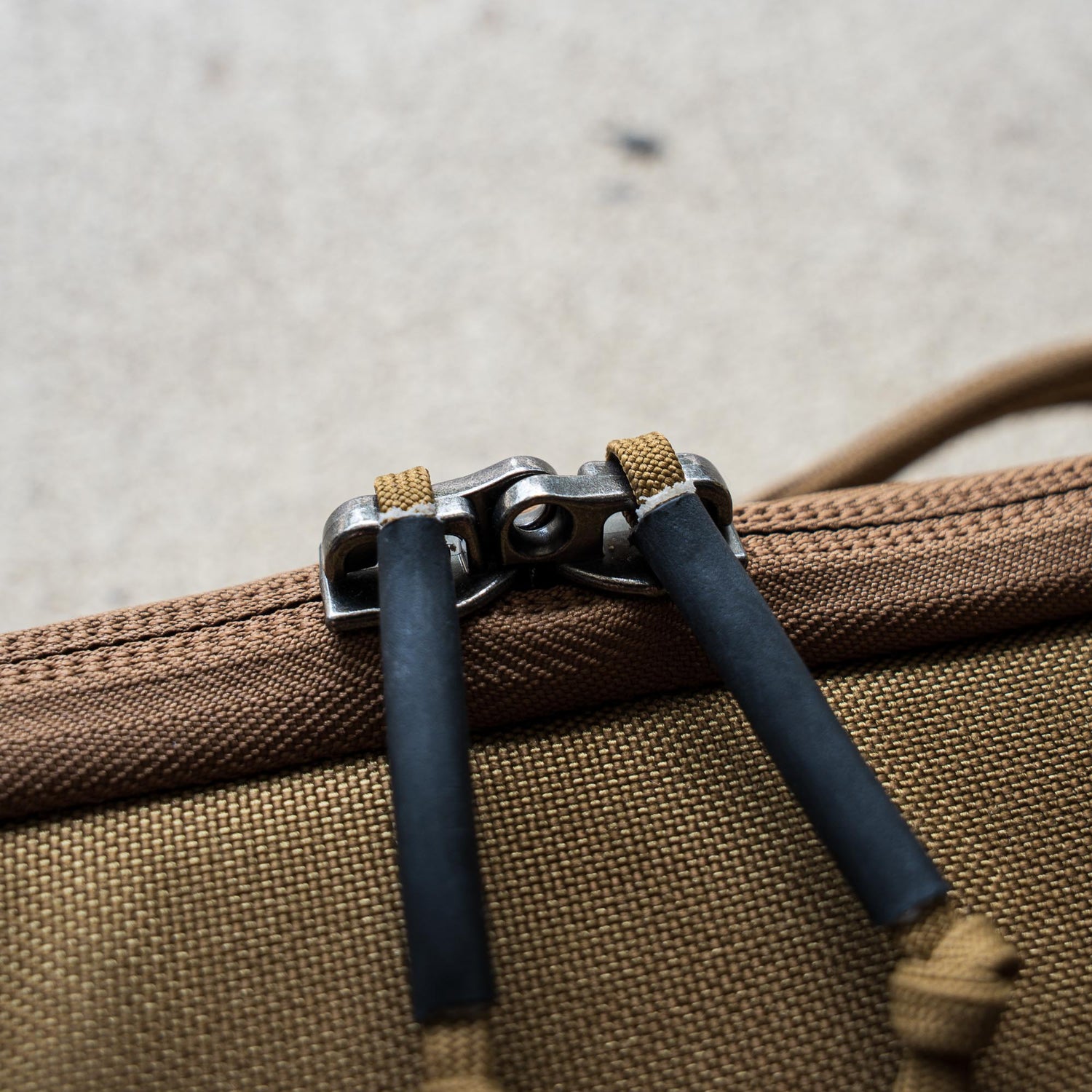 Close-up of a brown zipper with two black cord pulls on the textured fabric of a Rifle Case.