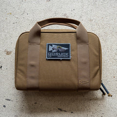 The brown Pistol Rug with handles and a "GORUCK Tactical" patch sits on a light textured surface—ideal as a modular pistol case or magazine pouch.