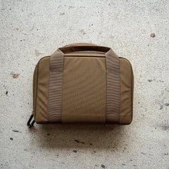 The Pistol Rug, a brown soft-sided modular pistol case with two handles, rests on a light textured concrete surface.