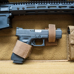 A black handgun secured with tan straps in foam, stored in the Retention Package beneath a larger firearm.