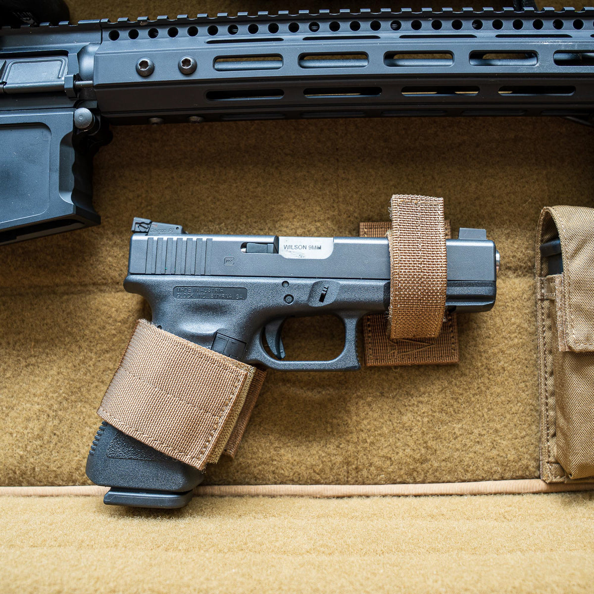 A Retention Package featuring a black handgun secured with brown straps inside a tan padded case, shown below part of a rifle.