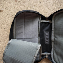 A black IFAK pouch with red thread, grey interior, and red patch (ROBIC w/ Aquaguard) featuring empty compartments lies open on a textured surface.