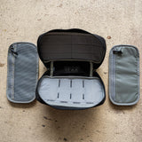 The IFAK (Black + Red Thread + Grey Interior + Red Patch) ROBIC w/ Aquaguard is open to show its gray pouches on each side, displayed on a textured beige surface.