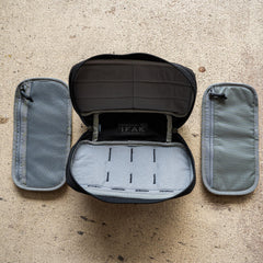 The IFAK (Black + Red Thread + Grey Interior + Red Patch) ROBIC w/ Aquaguard is open to show its gray pouches on each side, displayed on a textured beige surface.