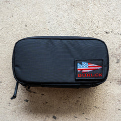 A black IFAK pouch (ROBIC) with red thread, grey interior, and a red patch, featuring an Aquaguard zipper, displayed on a textured surface.