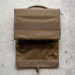 The Ammo Book is a brown fabric bullet organizer pouch with a handle and zippered pocket, shown open on a textured surface.