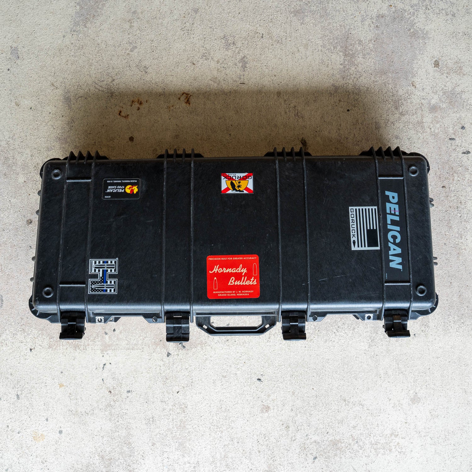 Black Rifle Case decorated with various colorful stickers, placed on a light concrete floor and viewed from above.