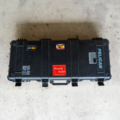 Black Rifle Case decorated with various colorful stickers, placed on a light concrete floor and viewed from above.