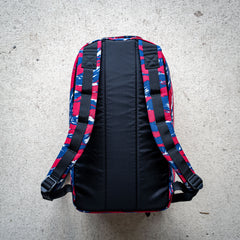 The Bullet Ruck Classic - Ballistic Nylon Cordura is a streamlined 15L daypack with blue, red, and white patterned straps and back, shown laid flat on a light concrete surface.