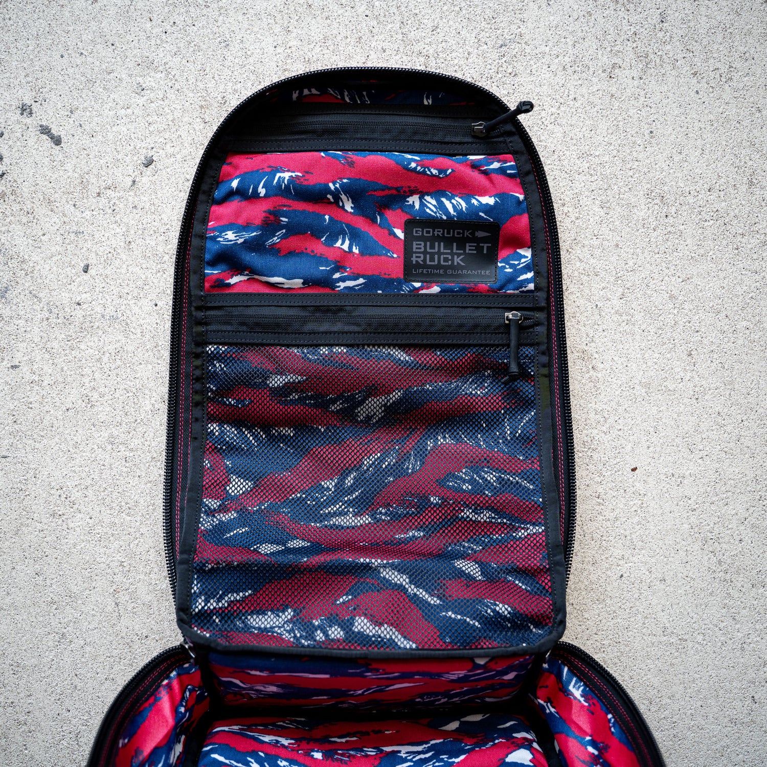 Open the Bullet Ruck Classic - Ballistic Nylon Cordura backpack, featuring a red, white, and blue camo interior with mesh pockets.