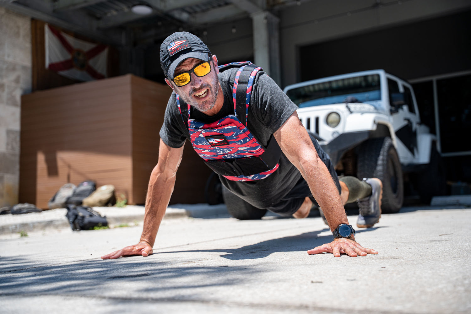 A man elevates his outdoor workout on a sunny day by doing push-ups near a white Jeep, wearing the Rucking Weight Vest.