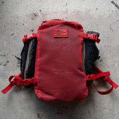 A red Mesh Ruck with black straps lies flat on a textured concrete surface.