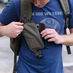 Man wearing GORUCK backpack opening green utility pouch on shoulder strap outdoors