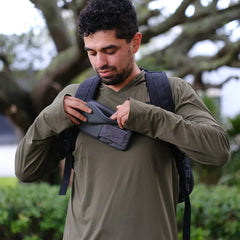 Man wearing GORUCK rucking backpack and khaki shirt, opening gear pouch outdoors