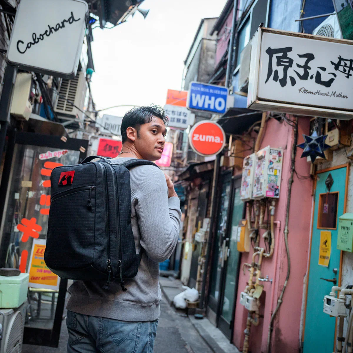 Man wearing a GORUCK backpack in a colorful urban alley with international signs