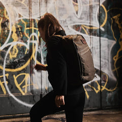 Woman with GORUCK dark oak rucksack in urban setting with graffiti background