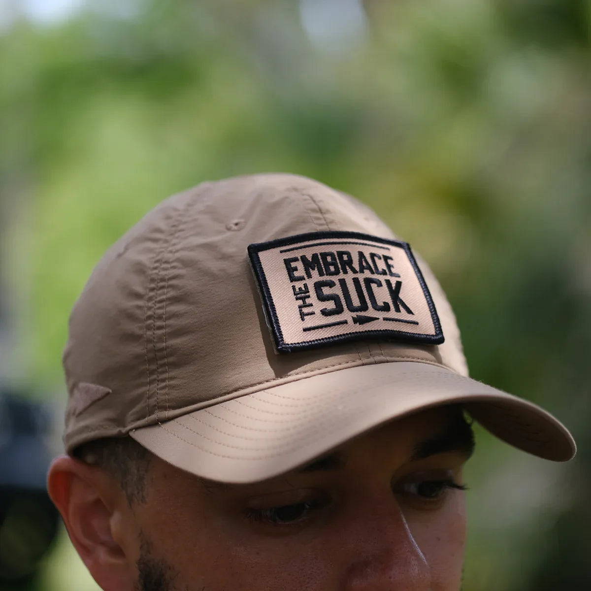 GORUCK tan cap with 'Embrace The Suck' patch outdoors, tough rucking gear closeup