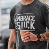 GORUCK charcoal tee with 'Embrace the Suck' text, man holding coffee, outdoor setting