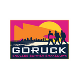 Three people with a surfboard walk past a city skyline at sunset with "GORUCK Endless Summer Shakedown" text, capturing the spirit of Ruckapalooza San Diego - Fitness Party & City Ruck Weekend, uniting the community for fitness and fun.