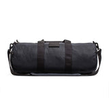 The Gym Bag - Waxed Canvas features classic black waxed canvas, two handles, a shoulder strap, and a minimalist design, all set against a white background.