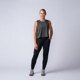 Woman in a gray sleeveless top, Women’s Training Performance Joggers, and sneakers stands and smiles against a plain background.