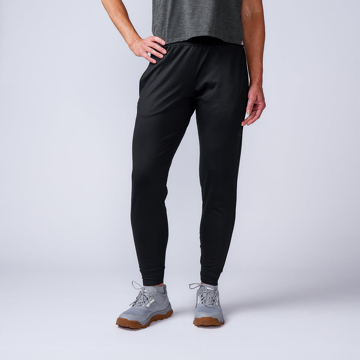 A person stands against a plain background wearing Women’s Training Performance Joggers in black, gray sneakers, and a dark gray t-shirt.