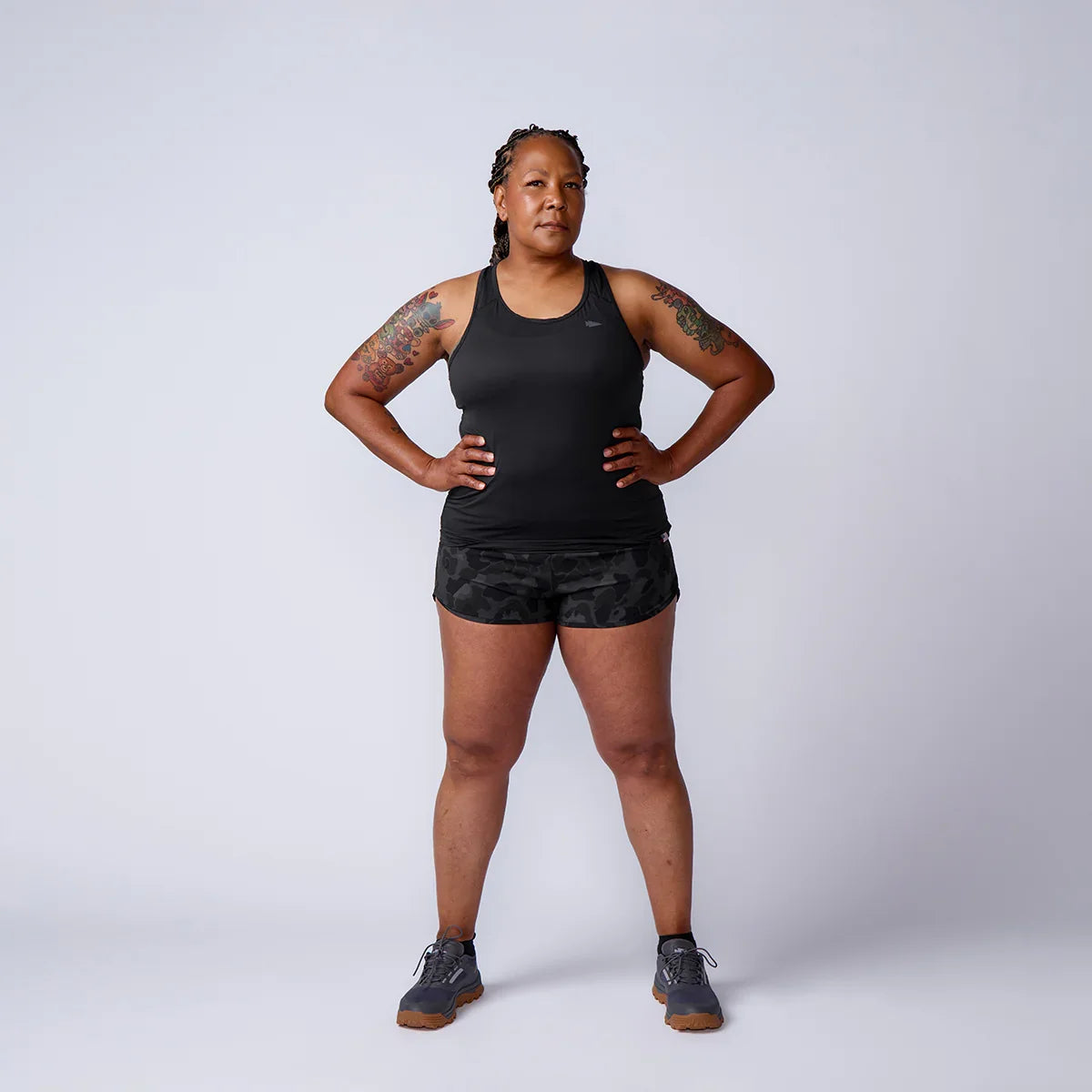 Athletic woman in GORUCK black tank top and camo shorts posing confidently in studio