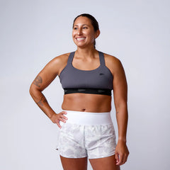 Smiling woman in gray GORUCK sports bra and camo shorts, studio background, rucking gear