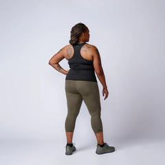 Woman in athletic GORUCK gear, black tank top, olive leggings, and sneakers, studio background