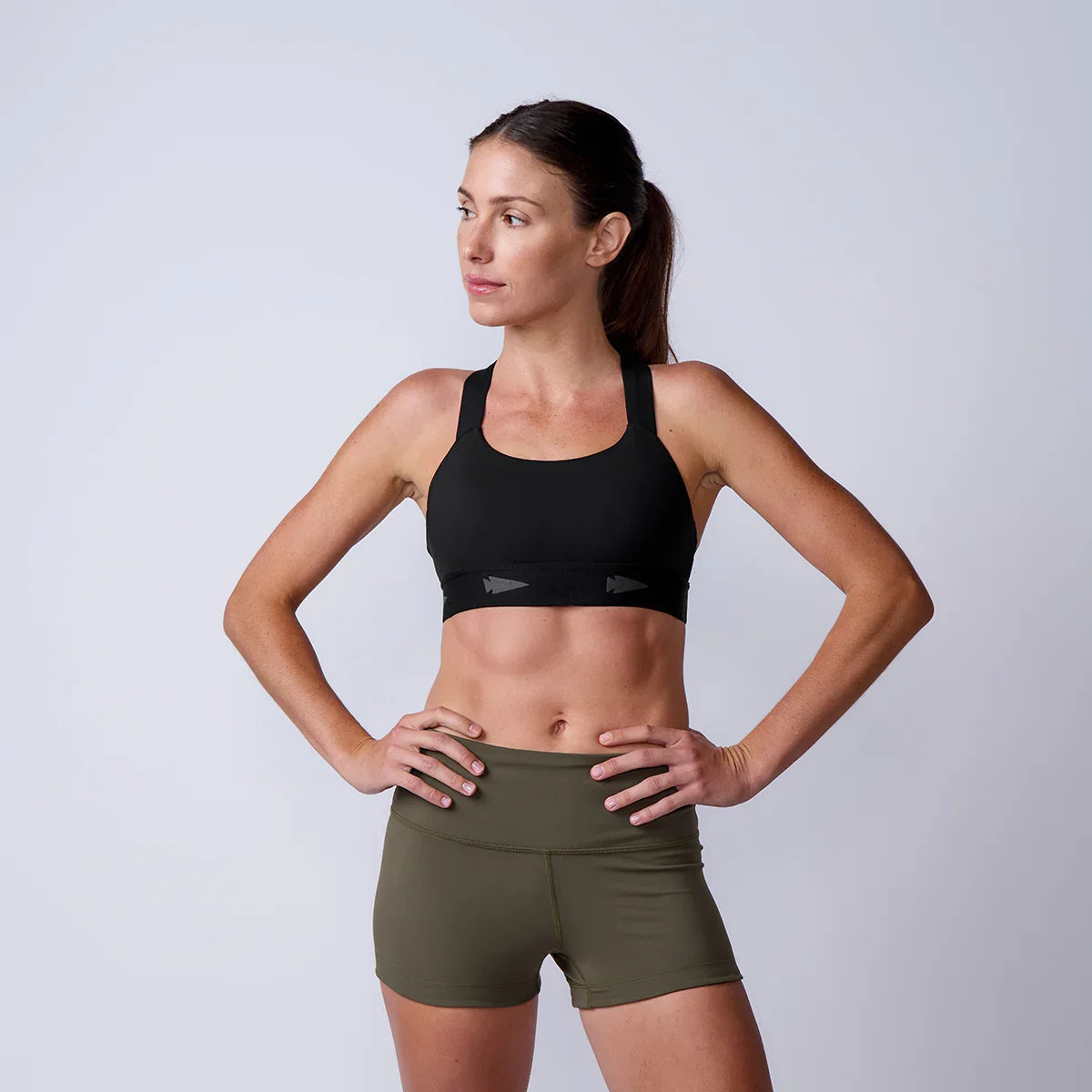 Woman in GORUCK athletic gear, wearing a black sports bra and olive green shorts, studio shot