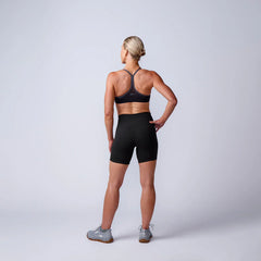Athletic woman in black GORUCK shorts and sports bra, standing in studio, rear view.