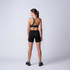 Woman in GORUCK rucking sports bra and shorts, back view, in minimalist studio setting