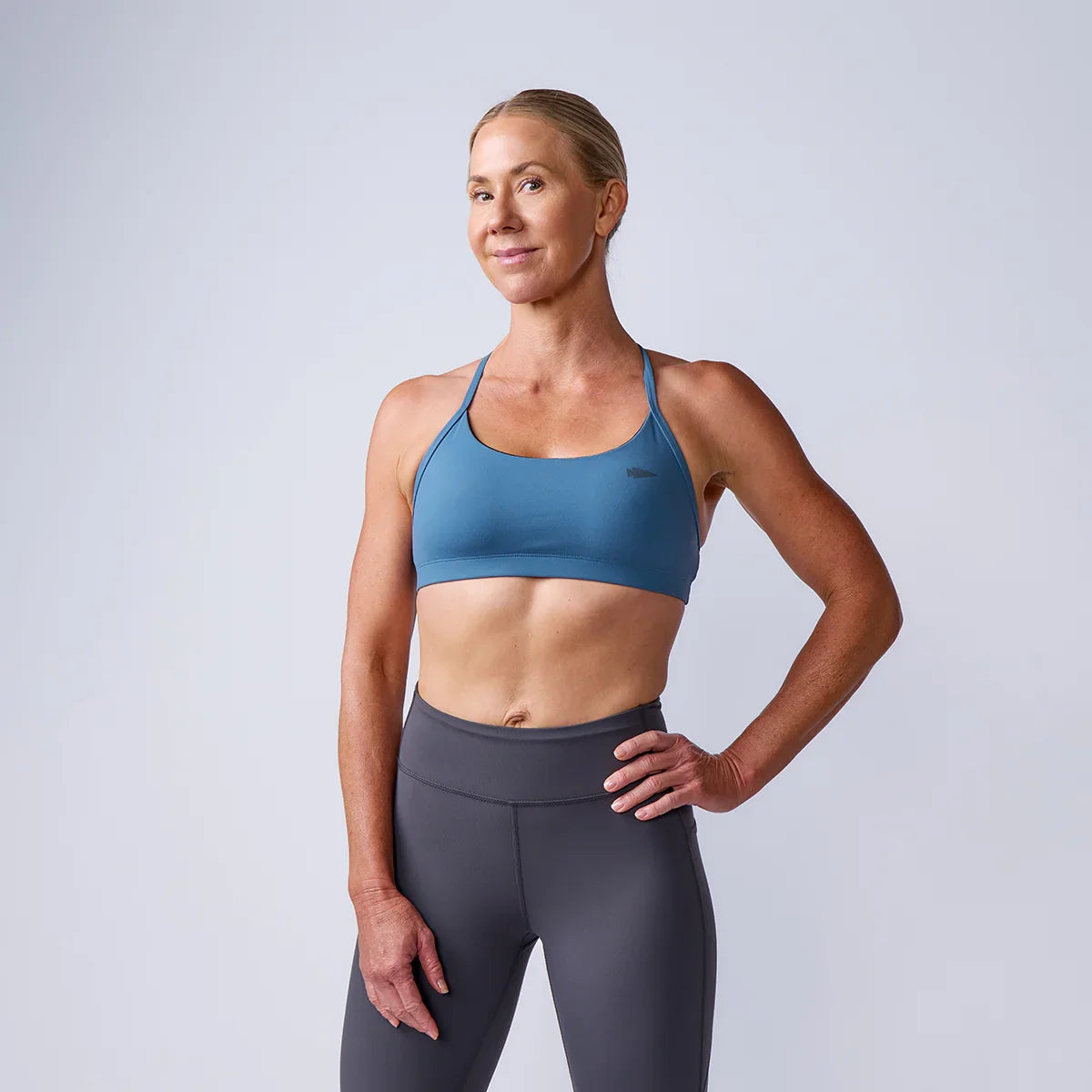 Woman in GORUCK athletic wear, blue sports bra and grey leggings, standing in studio
