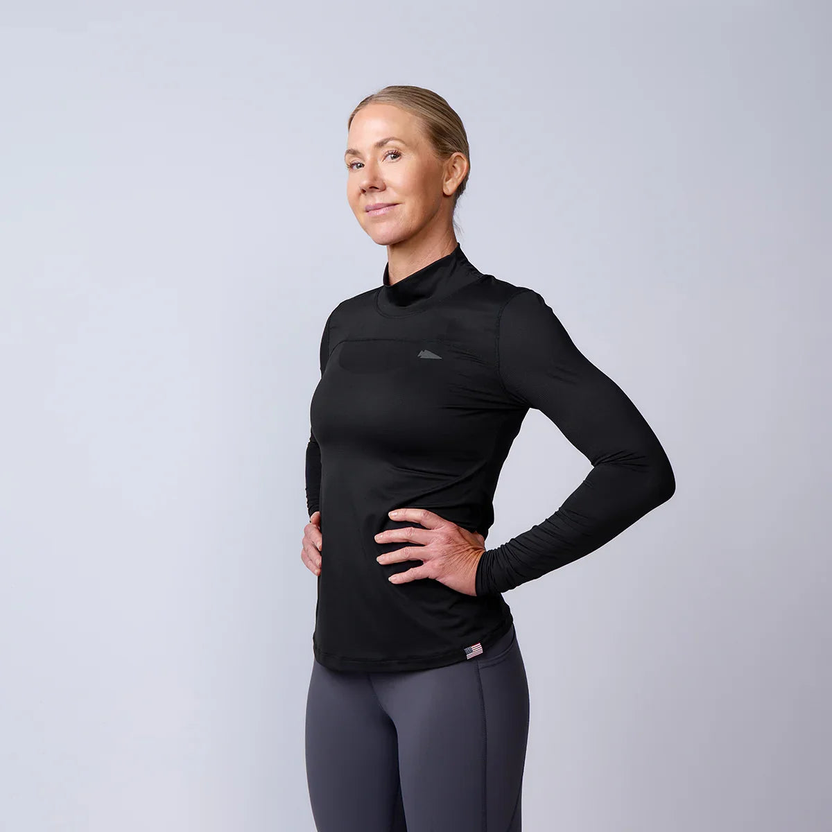 Woman wearing GORUCK black long sleeve rucking shirt and gray leggings on white background