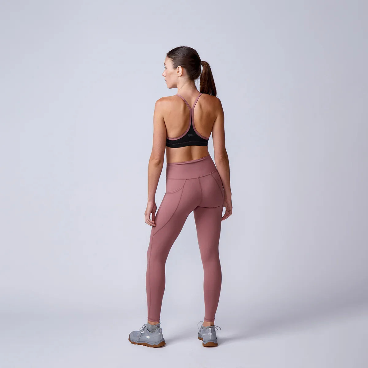 Woman in athletic wear facing away, wearing mauve leggings, sports bra, and GORUCK shoes