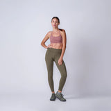 Woman wearing GORUCK olive green leggings, pink sports bra, and trail shoes in studio.