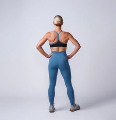 Woman wearing GORUCK blue athletic leggings and sports bra, standing in studio, back view