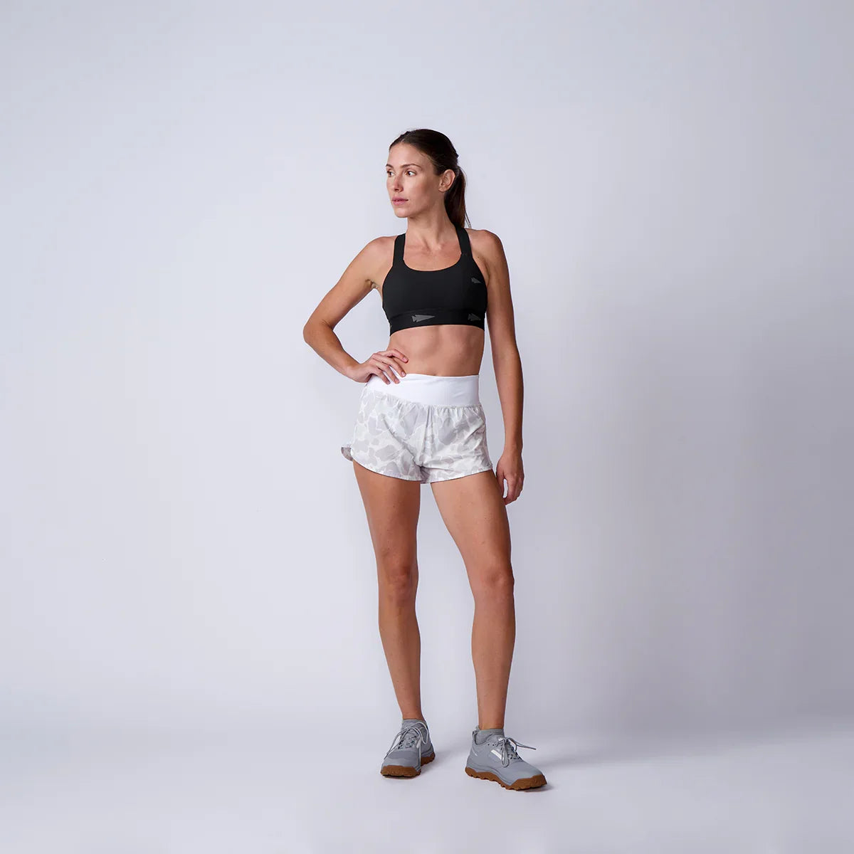 Woman wearing GORUCK athletic gear, black sports bra, camo shorts, grey rucking shoes in studio