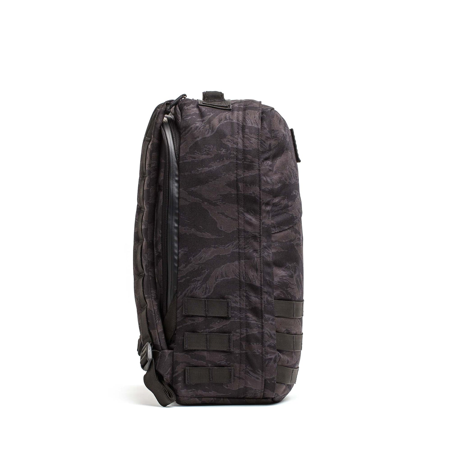 Side view of the GR1 USA - Cordura, a black and gray camouflage rucksack with Special Forces-grade MOLLE webbing and a top carry handle, inspired by the GORUCK Challenge.